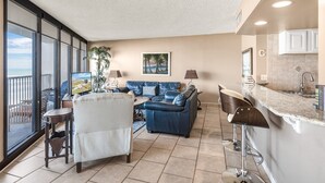 A living room with a blue sofa, a white armchair, and a dining area with a kitchen counter.