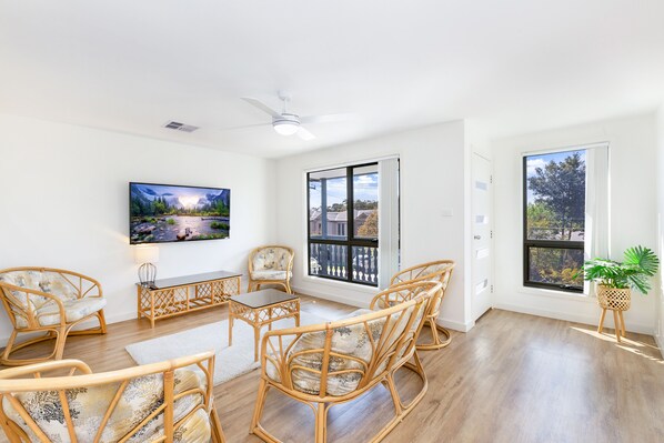 A spacious living room with a large flat-screen TV, wicker furniture, and a view through a sliding glass door. - AGATHAS  AT  MARION 
4 Bedrooms 3 with Ensuites  & 4th Bedroom Main Bathroom (Seacombe Gardens)