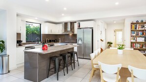A modern kitchen with a central island, bar stools, a dining table with chairs, a refrigerator, and a bookshelf. - AGATHAS  AT  MARION 
4 Bedrooms 3 with Ensuites  & 4th Bedroom Main Bathroom (Seacombe Gardens)