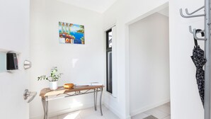 A bright hallway with a wooden table, a potted plant, a painting, and a coat rack. - AGATHAS  AT  MARION 
4 Bedrooms 3 with Ensuites  & 4th Bedroom Main Bathroom (Seacombe Gardens)