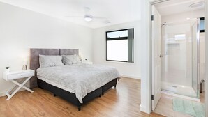 A bedroom with a bed, bedside tables, a nightstand, a window, and a glass-enclosed shower. - AGATHAS  AT  MARION 
4 Bedrooms 3 with Ensuites  & 4th Bedroom Main Bathroom (Seacombe Gardens)