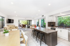 A modern kitchen with a central island, bar stools, a dining area with a table and chairs, and a living area with a sofa and chairs. - AGATHAS  AT  MARION 
4 Bedrooms 3 with Ensuites  & 4th Bedroom Main Bathroom (Seacombe Gardens)