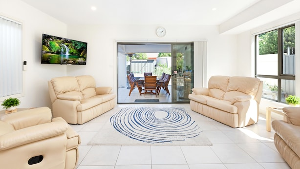 A modern living room with beige sofas, a flat-screen TV, and a dining area with a glass door leading outside. - AGATHAS  AT  MARION 
4 Bedrooms 3 with Ensuites  & 4th Bedroom Main Bathroom (Seacombe Gardens)