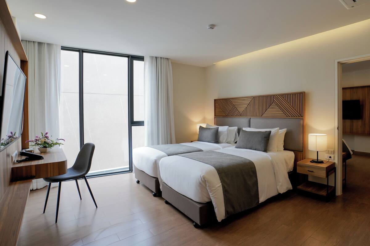 Une chambre d’hôtel moderne avec un grand lit, des tables de chevet, un bureau avec une chaise et une grande fenêtre.