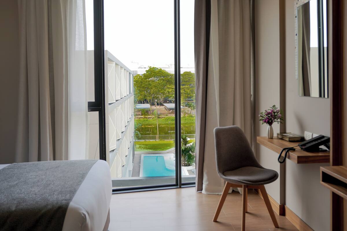 Une chambre d’hôtel avec un lit, une chaise, un bureau avec un téléphone et une vue sur une piscine et la verdure environnante.