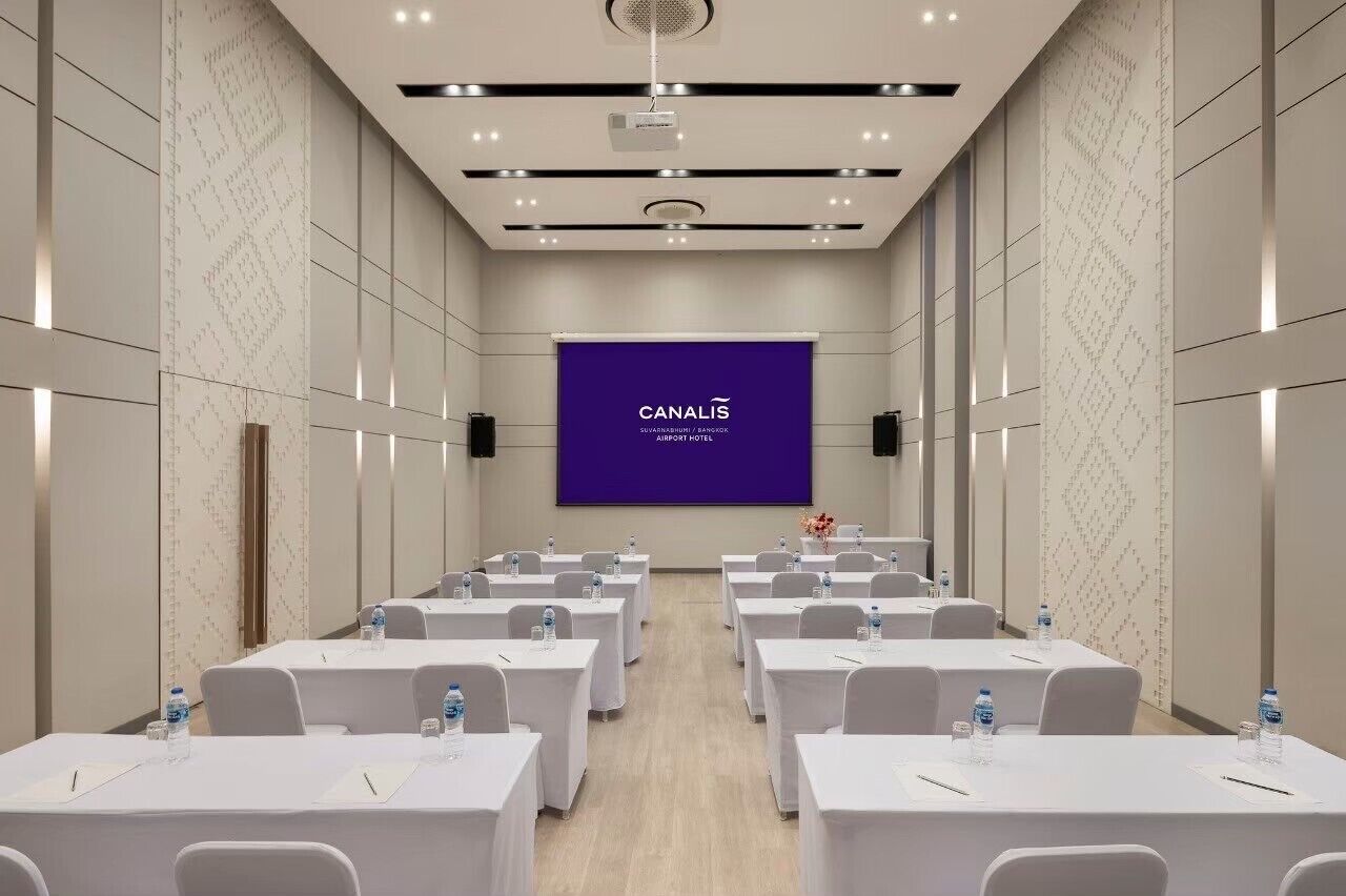 A conference room with rows of tables, a large screen displaying "CANALIS", and a projector on the ceiling.