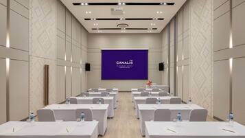 A conference room with rows of tables, a large screen displaying "CANALIS", and a projector on the ceiling.