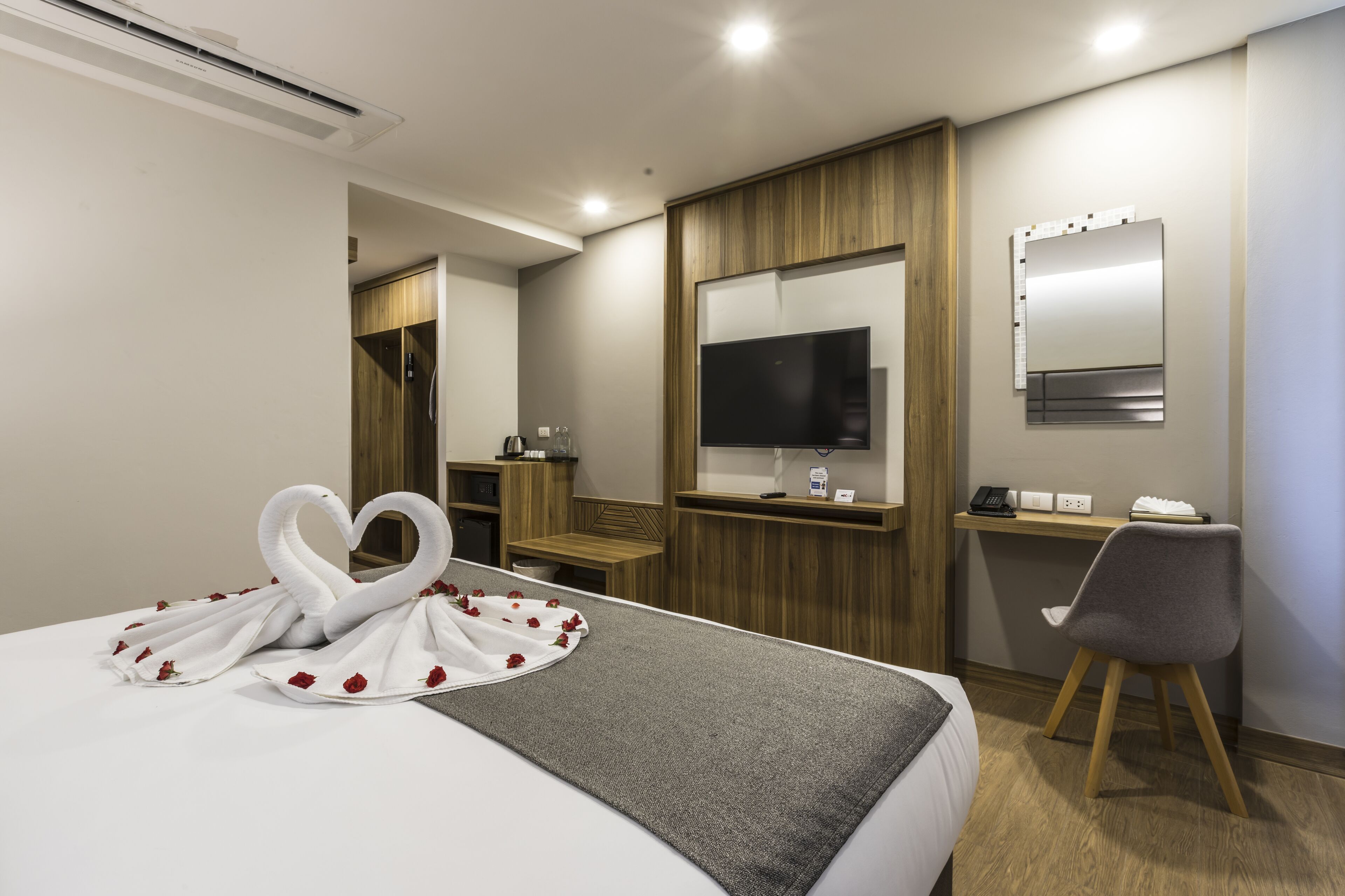 A hotel room with a bed, a desk, a chair, a TV, and a mirror.