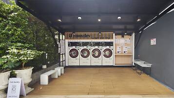 A coin laundry facility with four washing machines, a sign for Pier 13 Bistro & Cafe, and a sign for guestrooms B201 - B412.