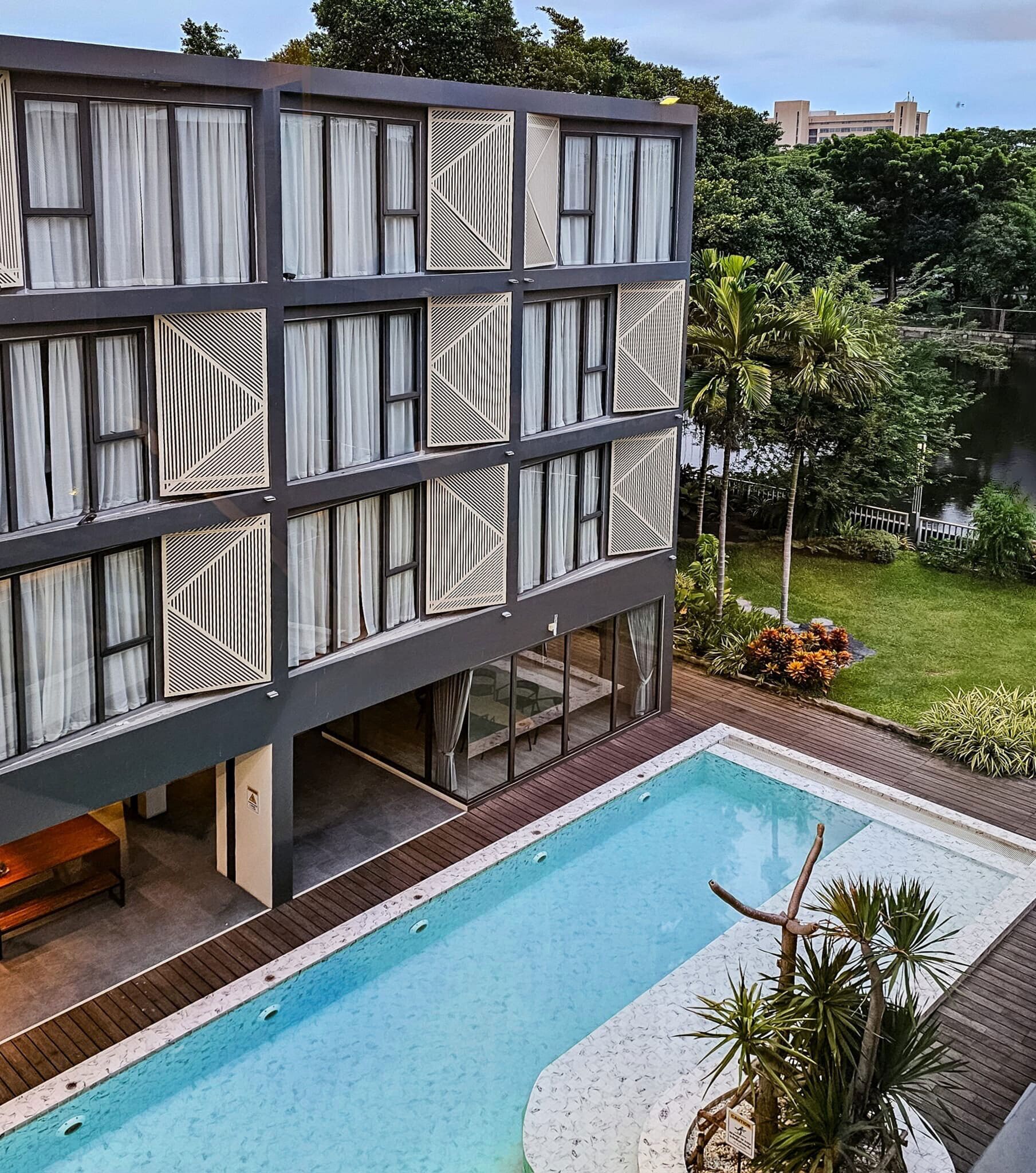 Un edificio moderno con piscina, destacando diseños geométricos en las ventanas y una terraza de madera.