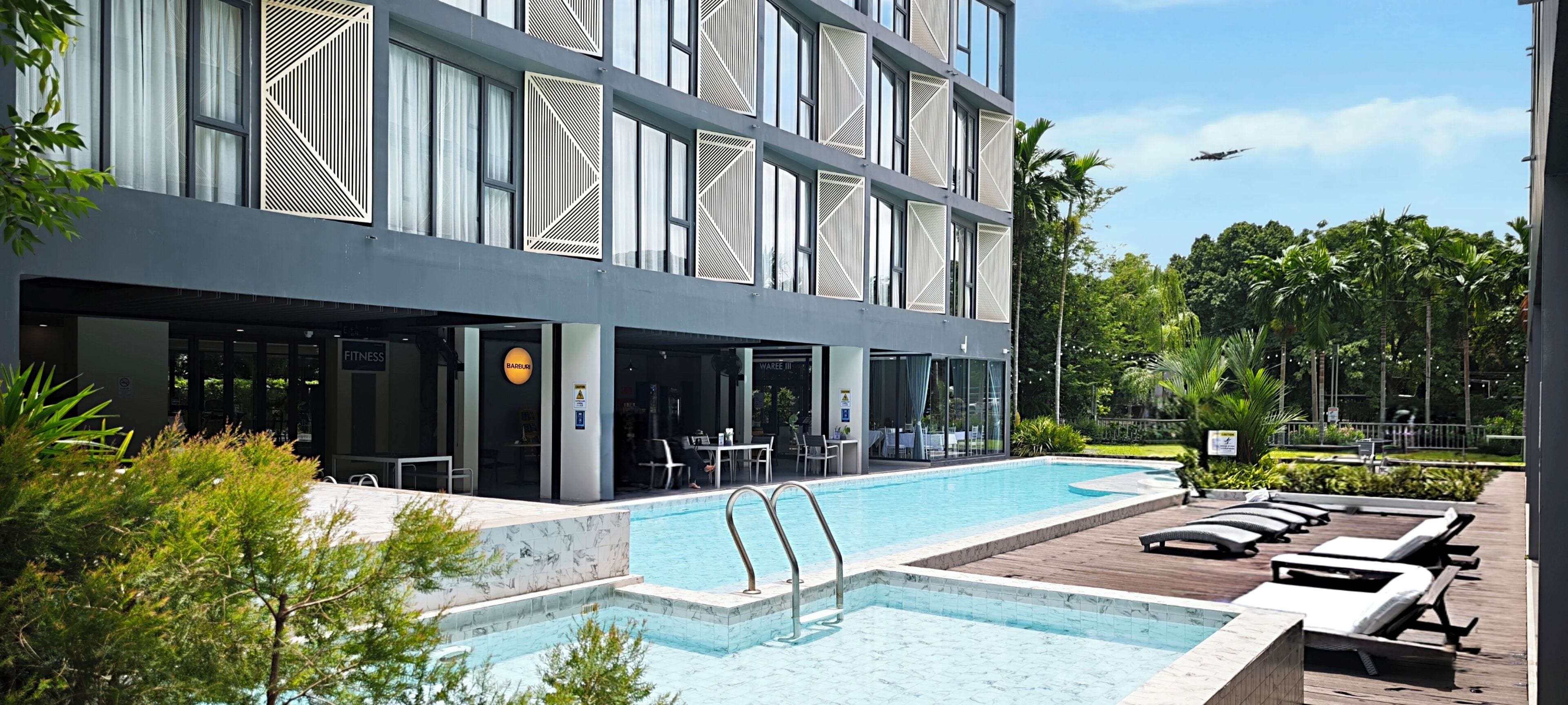 A modern building with a pool area, including lounge chairs and a dining area.