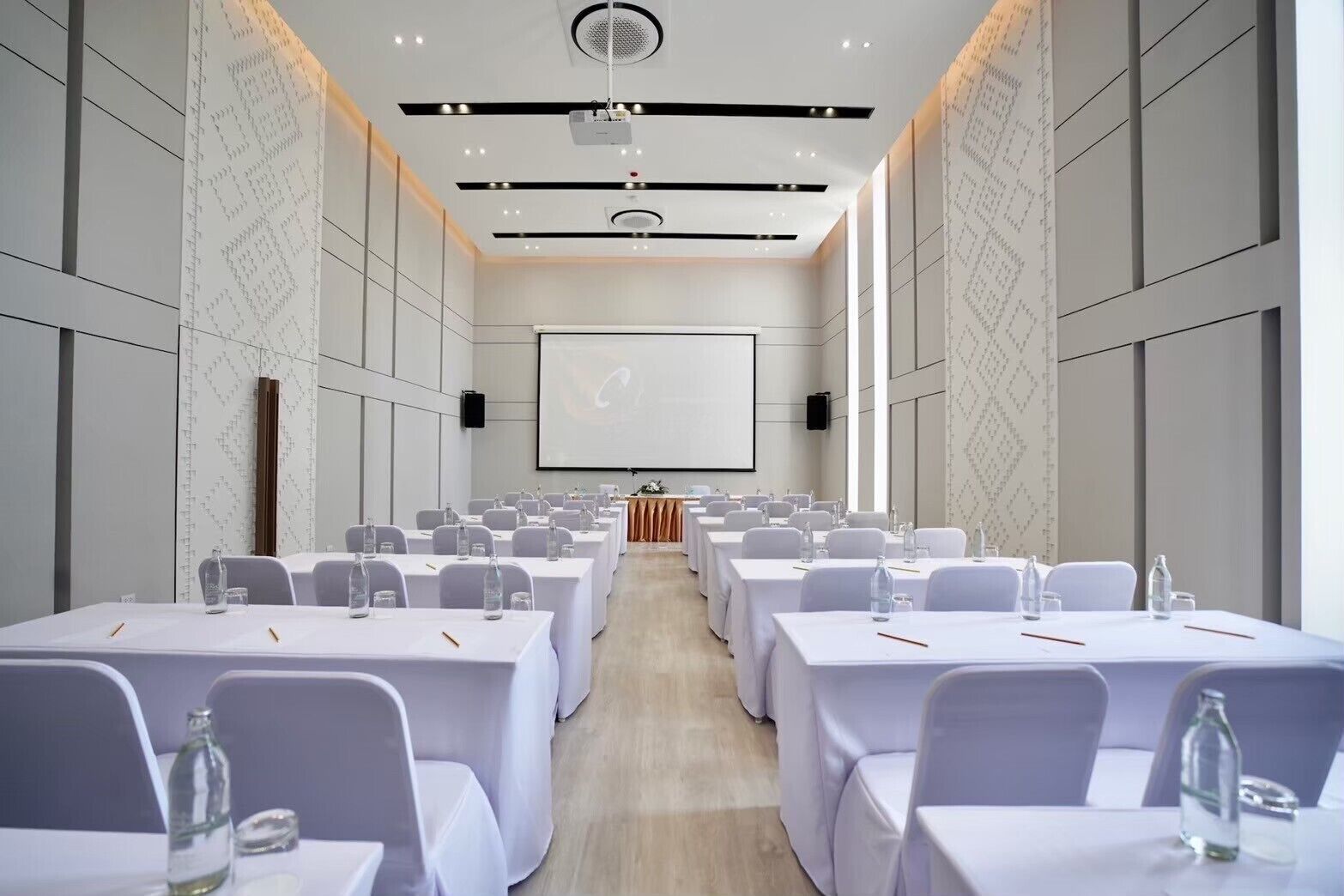 A conference room with rows of tables and chairs, a projector screen, and a wooden podium.
