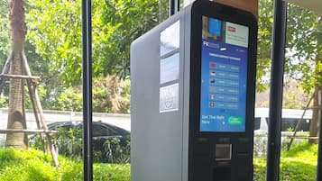 A currency exchange machine with a digital display, located indoors with a view of greenery outside.