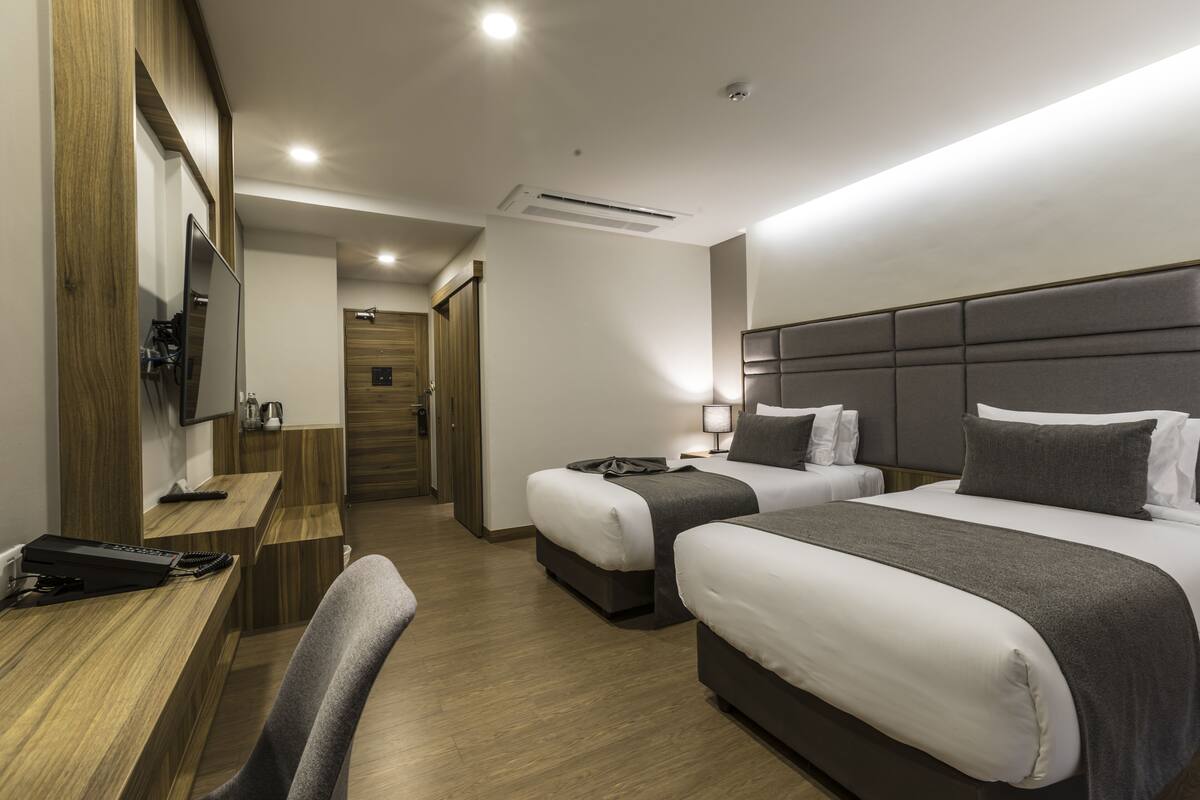 Une chambre d’hôtel avec deux lits, un bureau, une chaise, une télévision et un miroir.