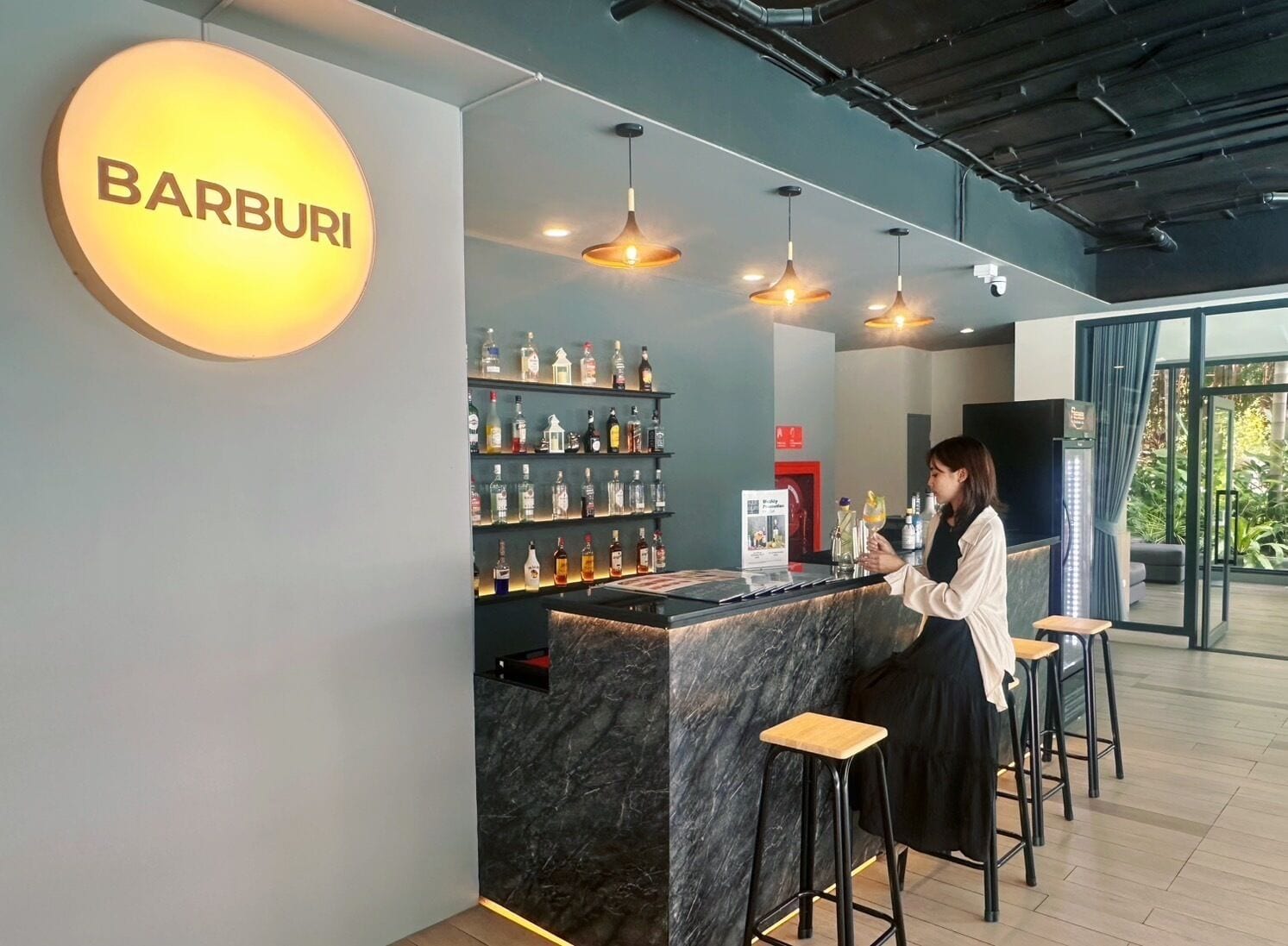 A bar area with a marble counter, shelves of liquor bottles, and hanging pendant lights.