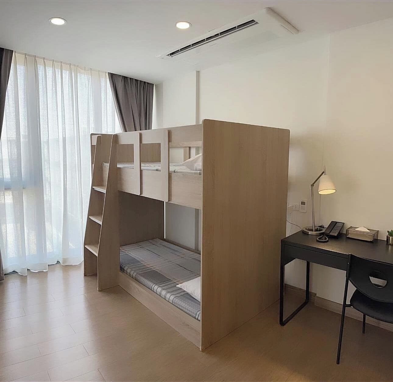 A compact room with a bunk bed, a desk with a lamp, and a chair.