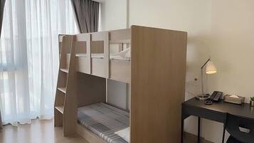 A compact room with a bunk bed, a desk with a lamp, and a chair.