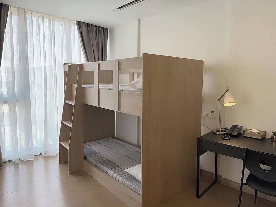 A compact room with a bunk bed, a desk with a lamp, and a chair.