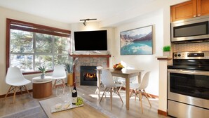 A modern living room with a fireplace, a dining area, and a kitchen with stainless steel appliances.