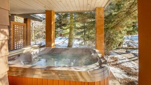 A hot tub under a wooden pergola with a snowy landscape in the background.