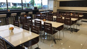 A modern dining area with multiple tables and chairs, large windows with a view of the street, and a flat-screen TV mounted on the wall. - Toyoko Inn Matsumoto-eki Higashi-guchi (Matsumoto)
