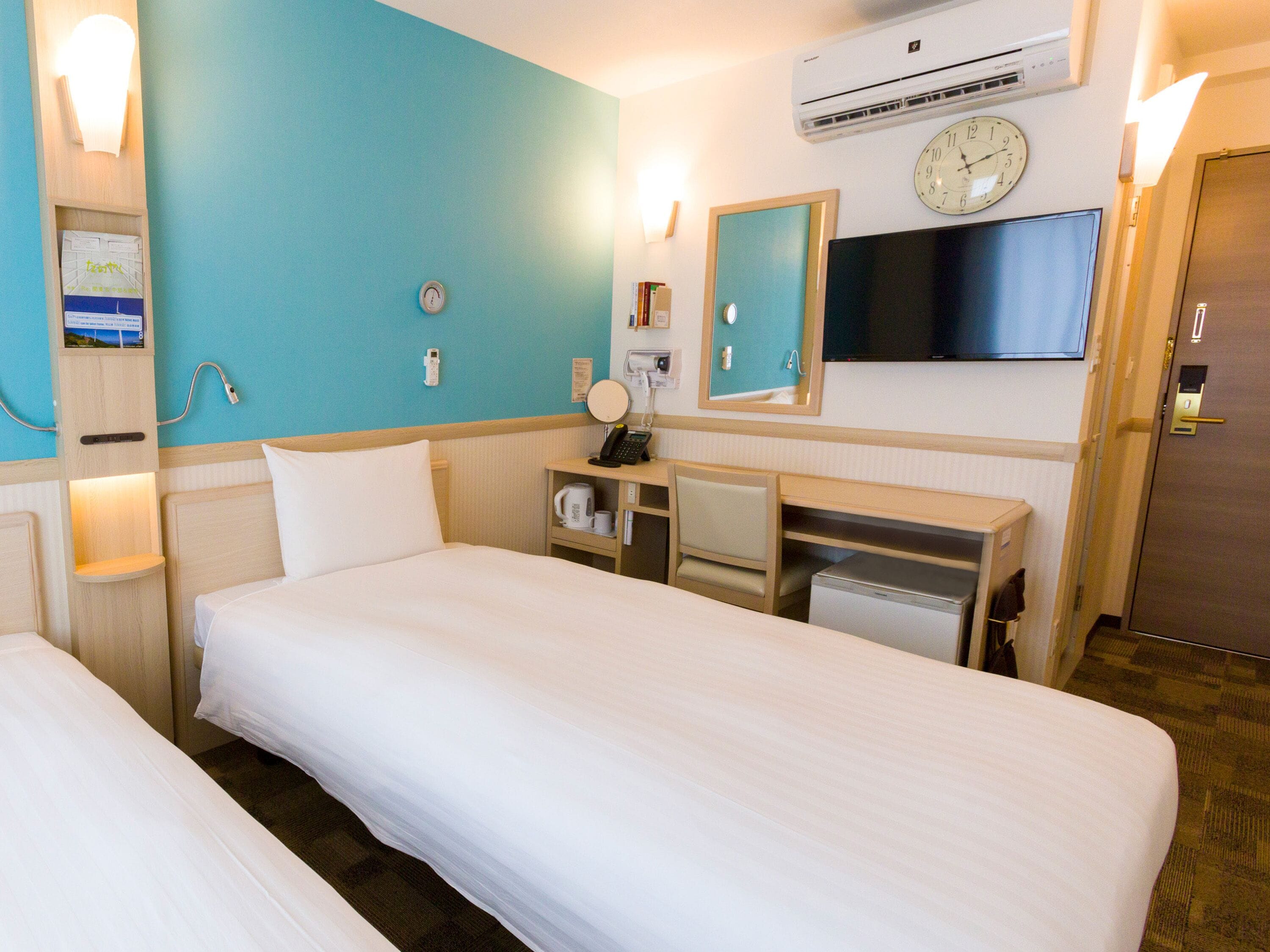 Habitación de hotel con dos camas, un escritorio, un espejo, un reloj y un aire acondicionado.