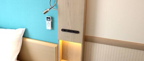 A hotel room with a bed, a bedside table with a lamp, a wall clock, and a telephone.