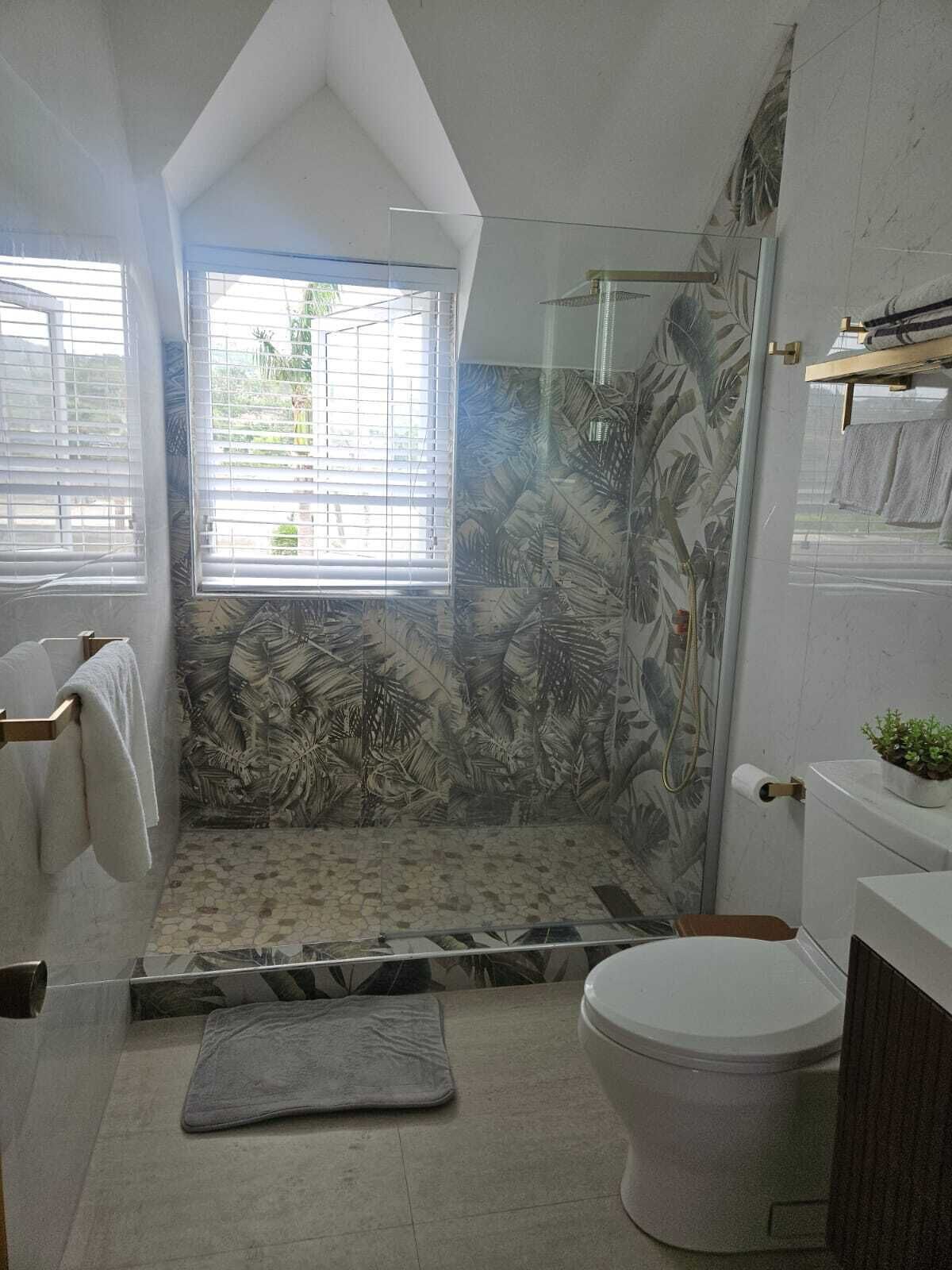 Un baño con ducha, inodoro y ventana con persianas.