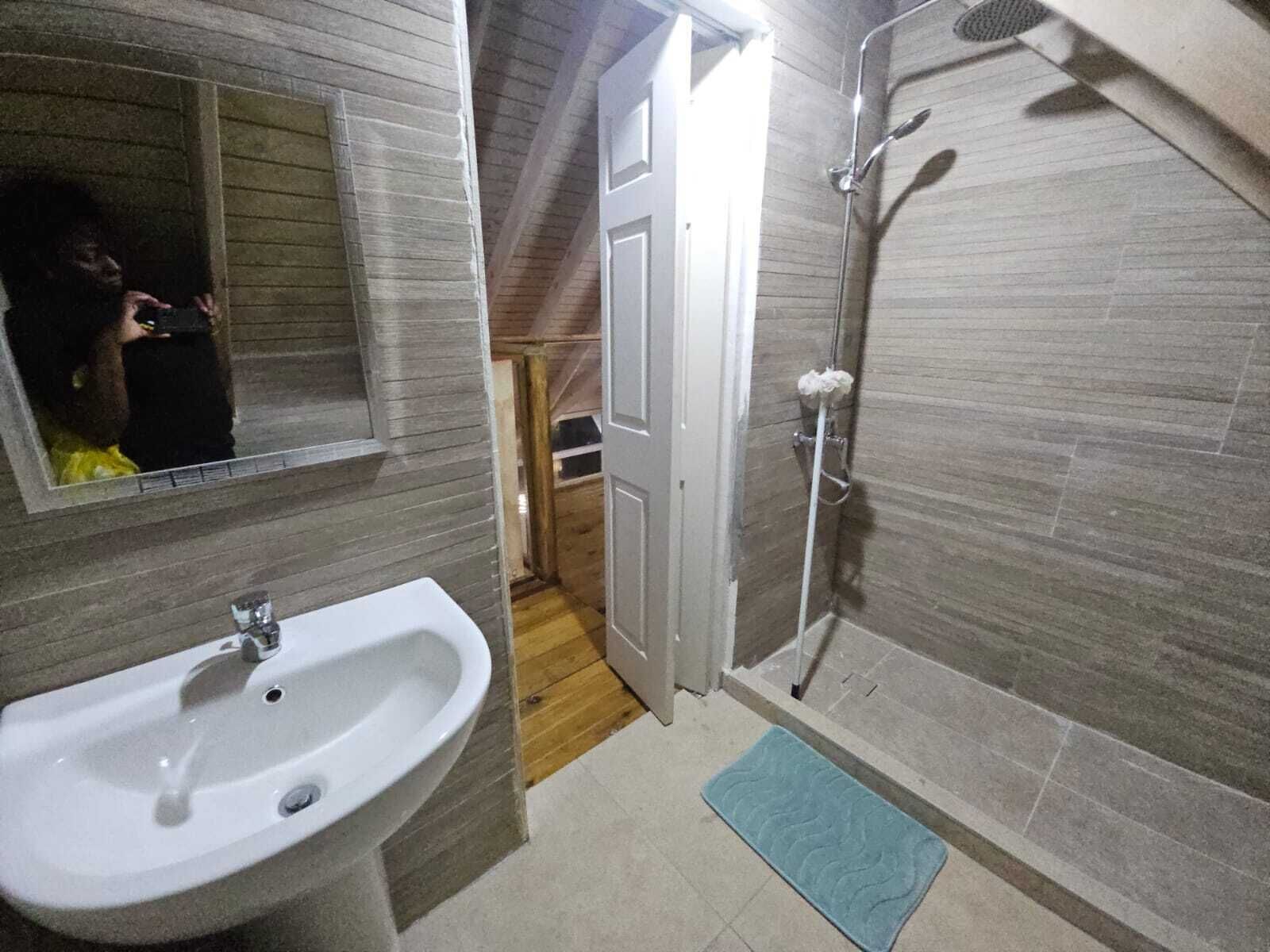 A bathroom with a sink, mirror, shower, and wooden flooring.