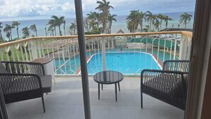 A balcony with a pool, chairs, and a view of the ocean and palm trees. - Seacastles Apartments (Montego Bay)
