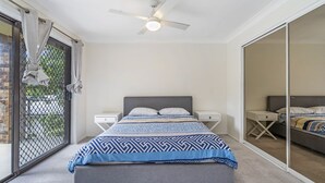 Un dormitorio con cama, mesitas de noche, ventilador de techo y puerta corrediza de vidrio a un balcón.