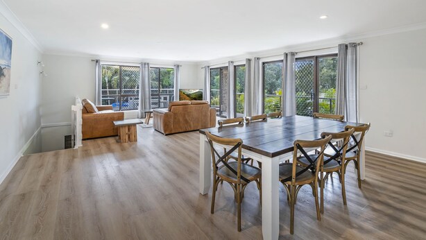 Un comedor amplio con una gran mesa de madera y sillas a juego, un sofá de cuero marrón y un televisor sobre un mueble.