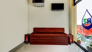 A modern room with a wooden sofa, a flat-screen TV, and a large window with a view of the city. - Itsy Hotels Rain Tulsi Stayz, Palarivattom Junction (Kanayannur)