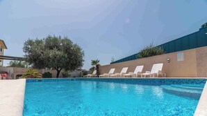 Ein klares, blaues Schwimmbecken mit weißen Liegestühlen und einer Palme im Hintergrund.