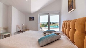 Ein Schlafzimmer mit einem großen Bett, Meerblick durch eine Schiebetür und einem Gemälde an der Wand.