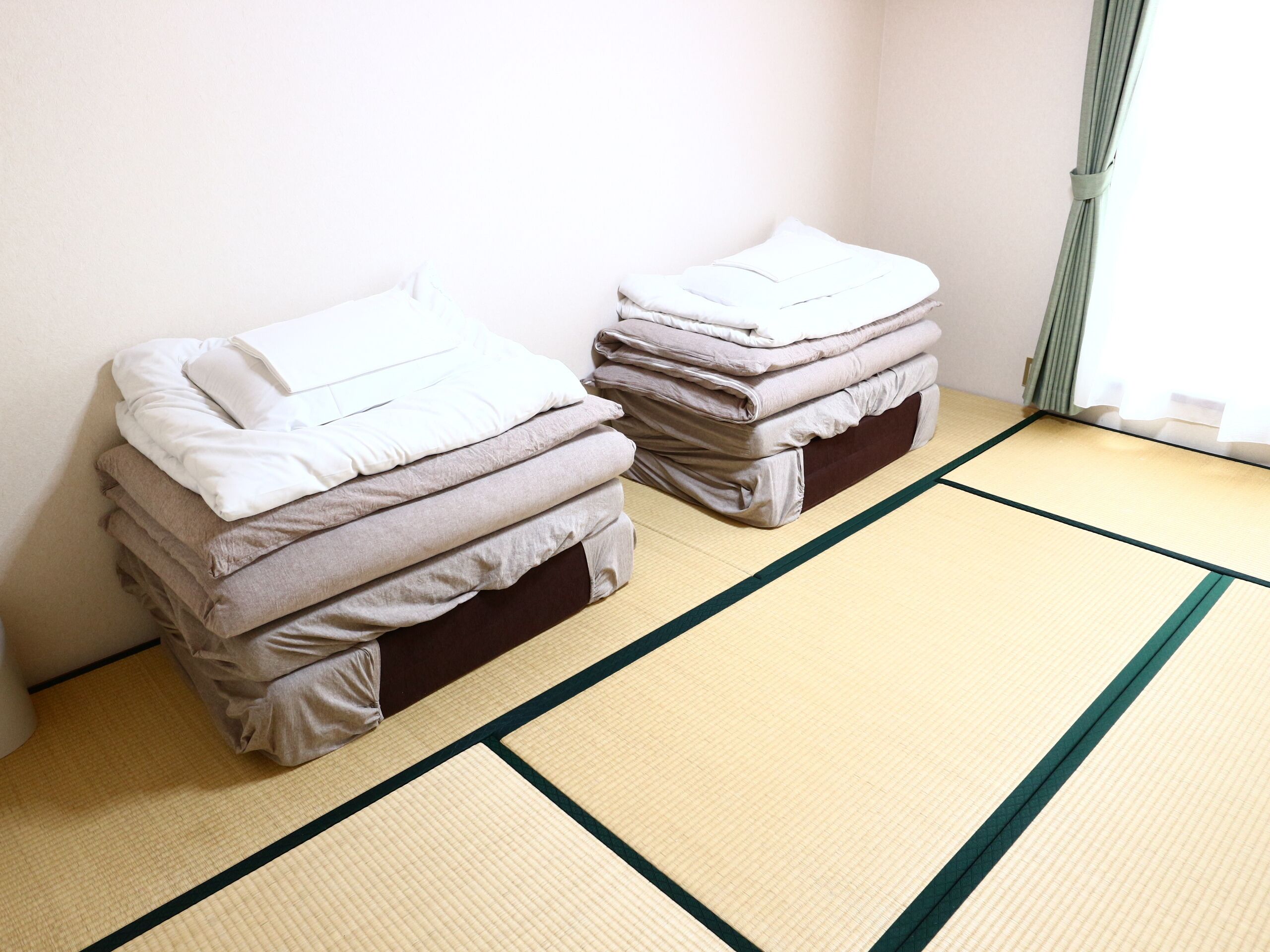 Dos camas con ropa de cama doblada en una habitación con suelo de tatami.