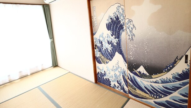 A room with tatami flooring, a sliding shoji screen with a wave painting, and a ceiling-mounted air conditioning unit. - Fujisan YOU Apartment (Fujiyoshida)