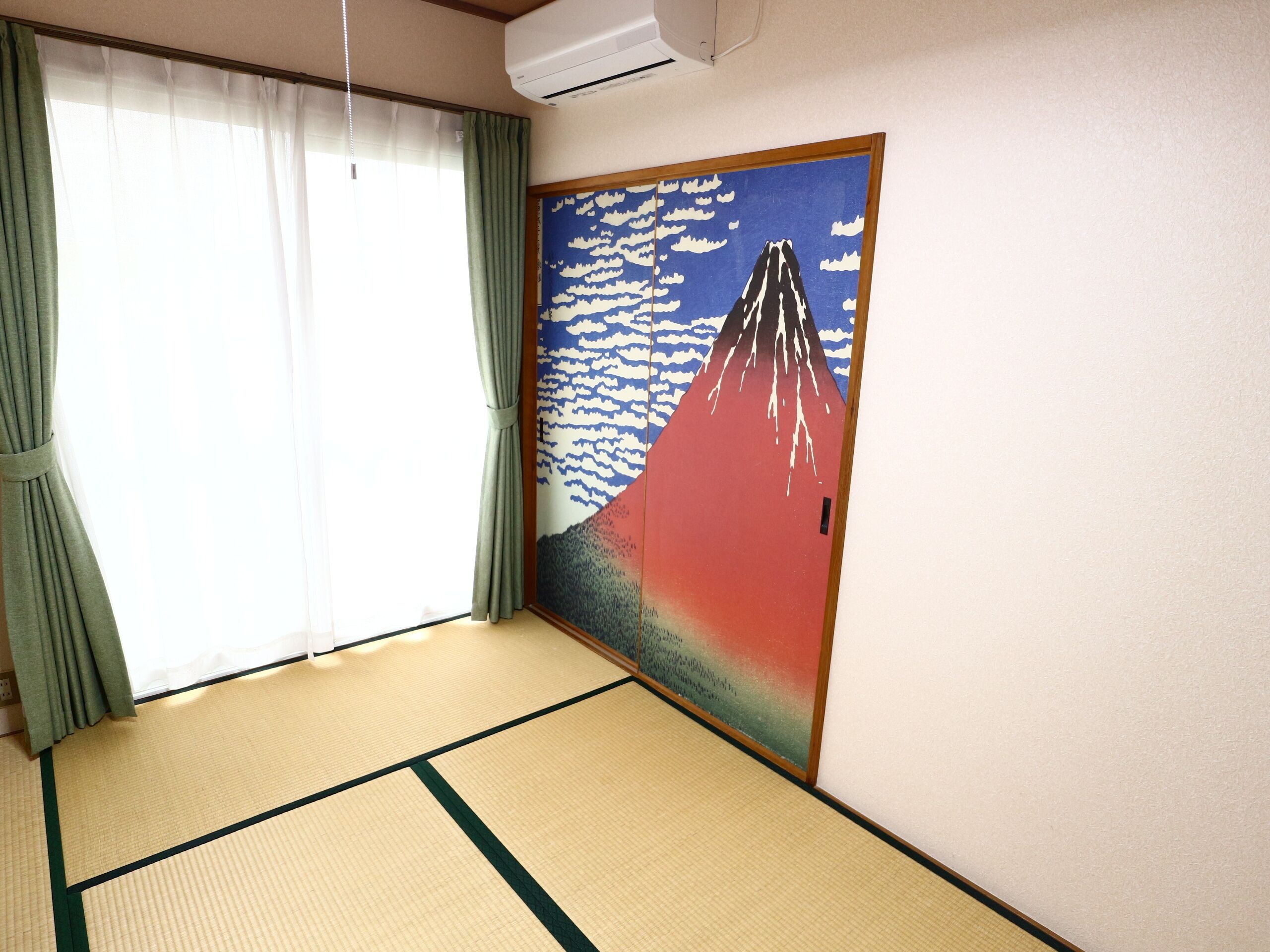 A room with tatami mat flooring, a large painting of Mount Fuji, and a sliding door with green curtains.