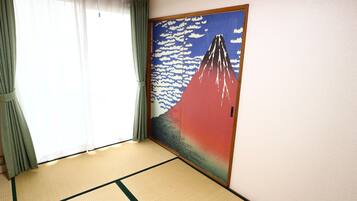 A room with tatami mat flooring, a large painting of Mount Fuji, and a sliding door with green curtains.