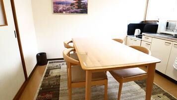 A small, clean room with a wooden dining table, chairs, a kitchen area, and a framed picture of a pagoda on the wall.