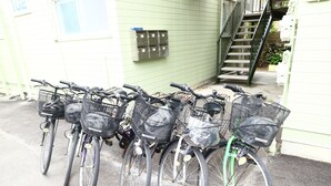 A row of bicycles parked in front of a building with a green exterior and a staircase. - Fujisan YOU Apartment (Fujiyoshida)