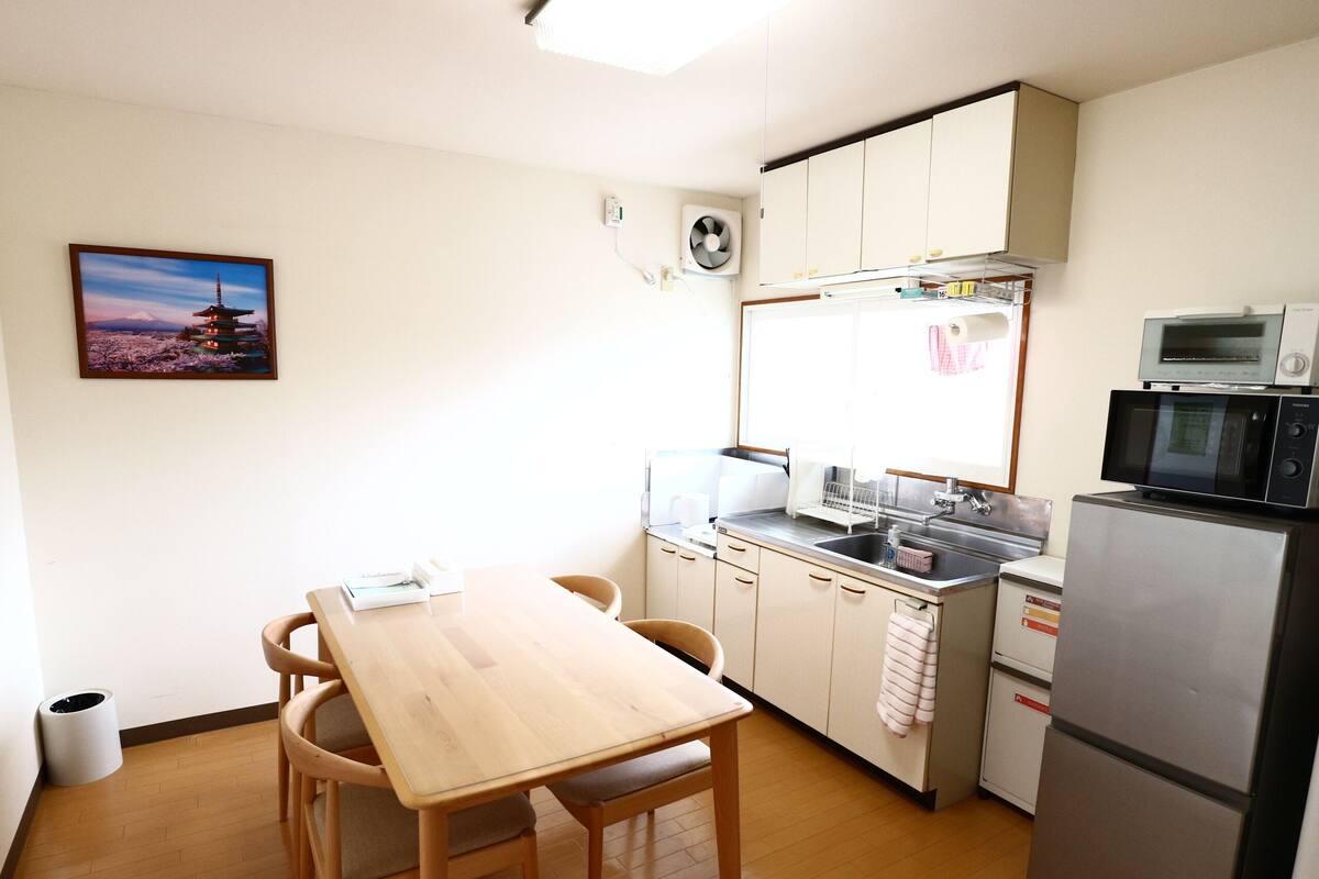 Una pequeña cocina con una mesa de madera, sillas, un refrigerador, un microondas y un lavaplatos.
