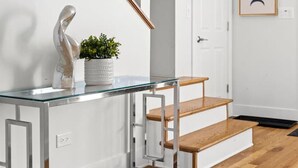 A modern interior with a glass console table, a wooden staircase, and a door with a framed artwork. - Stunning 6 BR Home * Chicago * Centrally Located (Chicago)