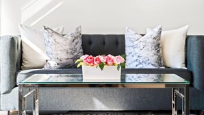 A modern living room with a grey sofa, marble-patterned cushions, and a glass coffee table with a vase of pink flowers. - Stunning 6 BR Home * Chicago * Centrally Located (Chicago)