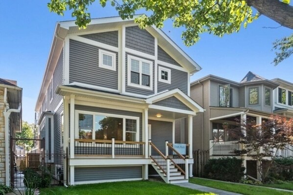 A two-story residential building with a front porch, a garage, and a staircase leading to the second floor.