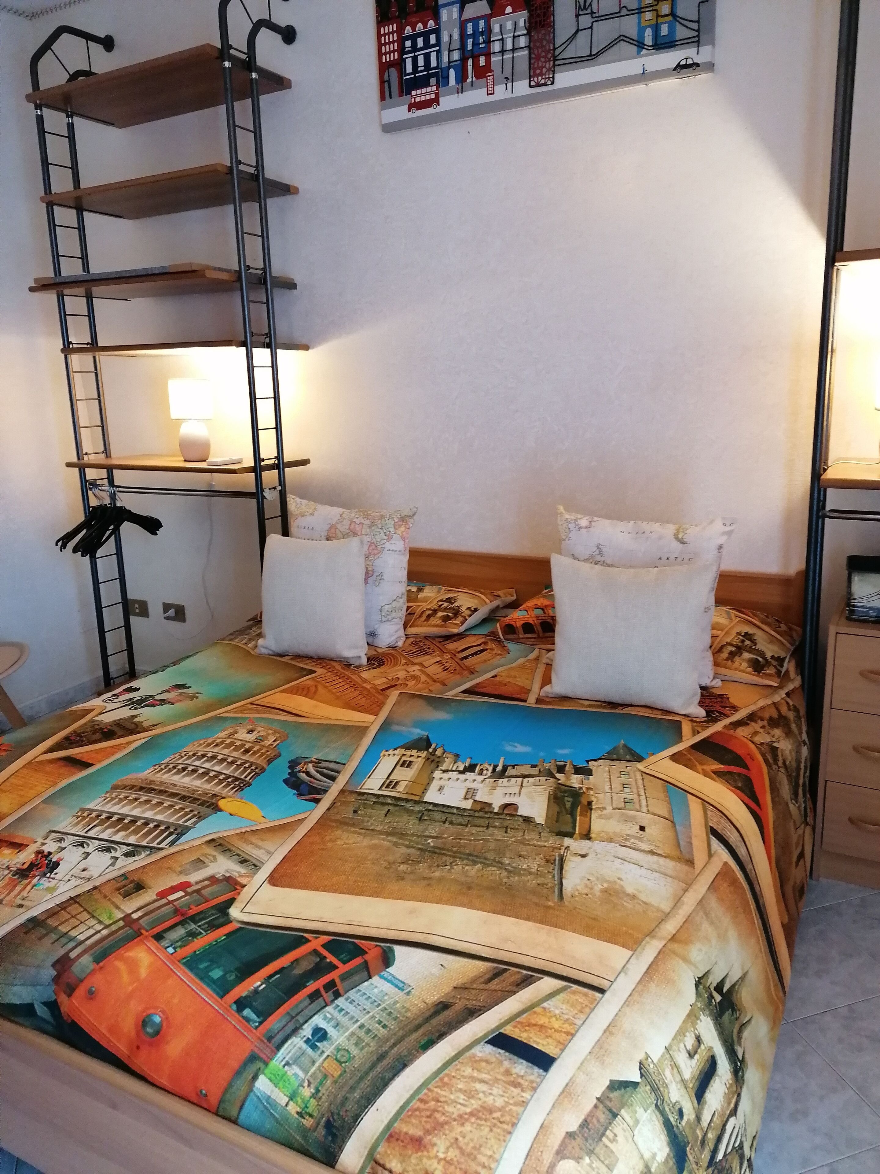 A bed with a colorful travel-themed bedspread, a ladder, and a map on the wall.