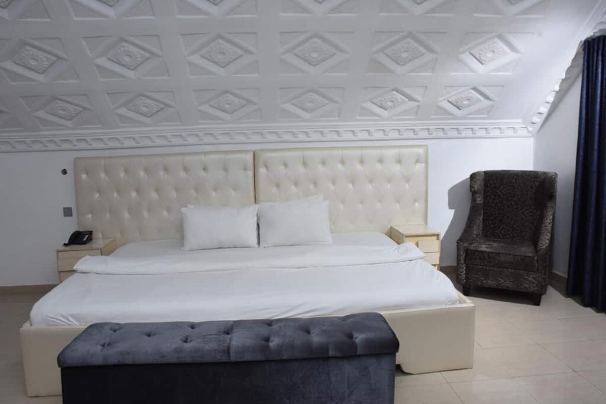 A bedroom with a tufted headboard, a large bed, a bedside table with a lamp, a chair, and a bench.