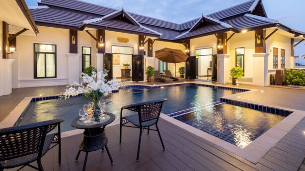 Una villa moderna con piscina, mobiliario exterior y un patio cubierto.