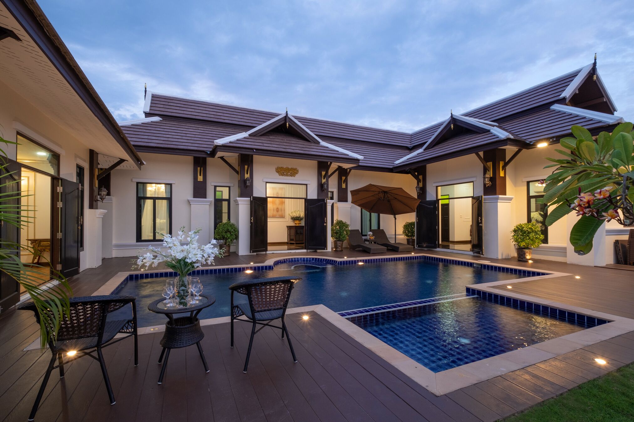 Una casa moderna con piscina, mobiliario de exterior y un patio bien iluminado.