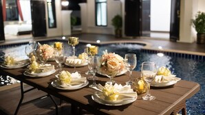 Una mesa de comedor dispuesta con platos, vasos y centros de mesa con flores al lado de una piscina.